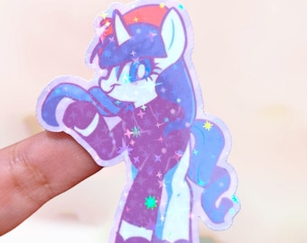 Op de afbeelding: Een glimmende paarse en blauwe unicorn sticker met een rode hoed en witte sterren. De unicorn draagt een paarse en witte outfit.