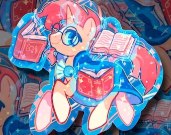 May include: A sticker featuring a cartoon unicorn with glasses, holding and surrounded by books. The unicorn has pink hair and is wearing a blue cloak. The sticker has a blue and pink color scheme with glitter accents.