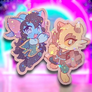 Puede incluir: Dos pegatinas de personajes de dibujos animados, una azul con orejas de murciélago y un atuendo verde, la otra amarilla con orejas de zorro y un atuendo marrón. Ambos personajes tienen detalles brillantes.