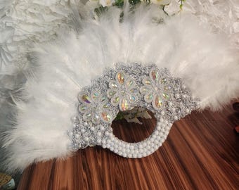 May include: A white feather fan with a silver and white beaded handle and silver embellishments. The fan is closed and has a pearl-like bead trim.