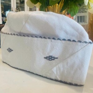 May include: White cotton skullcap with a blue embroidered design. The skullcap has a scalloped edge.