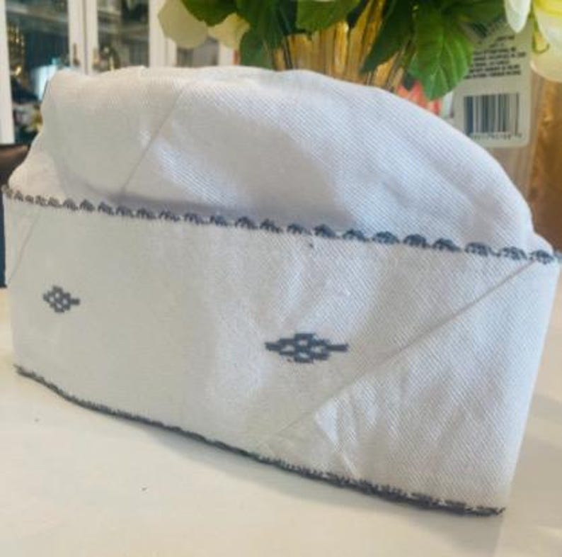 May include: White cotton skullcap with a blue embroidered design. The skullcap has a scalloped edge.