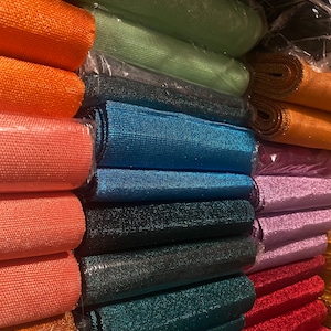 Può includere: Una varietà di rotoli di nastro scintillanti e colorati impilati su uno scaffale. I rotoli sono in tonalità di arancione, verde, blu, nero, turchese, rosso e viola.