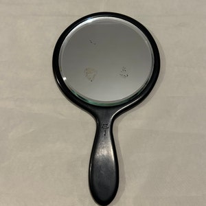 May include: A black hand mirror with a round mirror and a black wooden handle.