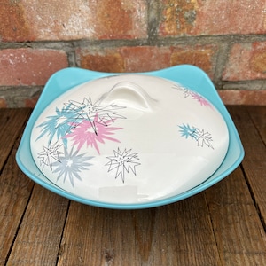 May include: A vintage blue and white ceramic serving dish with a lid. The lid features a stylised floral design in pink, blue and black.