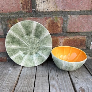 May include: Two ceramic bowls with a melon design. One bowl is green and the other is orange with a green rim.