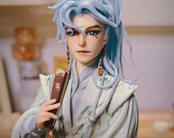 May include: A hand-crafted figurine of a person with long blue hair, wearing a white and green patterned robe and holding a book. The figurine is made by "WAIFU 2X" and is labeled "Hand Made with Love".