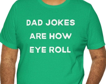 May include: A green t-shirt with the text "DAD JOKES ARE HOW EYE ROLL" in white. The shirt is being worn by a person smiling at the camera. The person is wearing black pants.