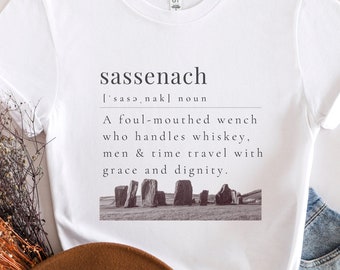 May include: White t-shirt with a graphic design that reads "sassenach ['sasənak] noun A foul-mouthed wench who handles whiskey, men & time travel with grace and dignity." The graphic also includes a black and white image of a stone circle.