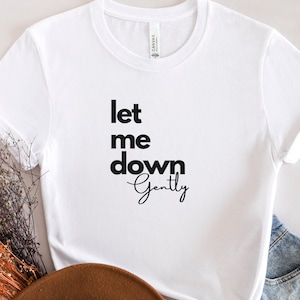 May include: White t-shirt with black text that reads "let me down gently".