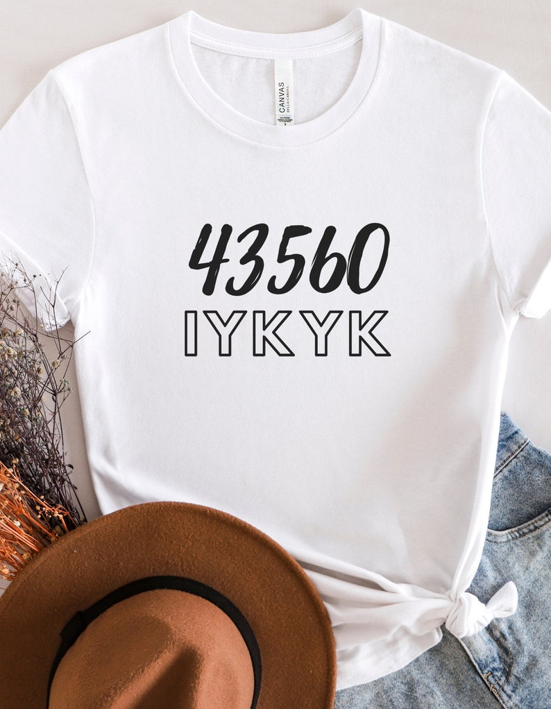 以下が含まれることがあります： 黒い文字で「43560 IYKYK」と書かれた白いTシャツ。