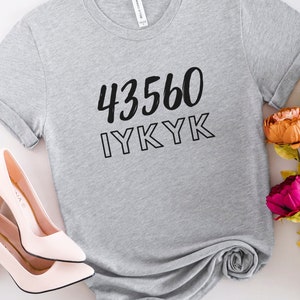 以下が含まれることがあります： 黒い文字で「43560 IYKYK」と書かれたグレーのTシャツ。