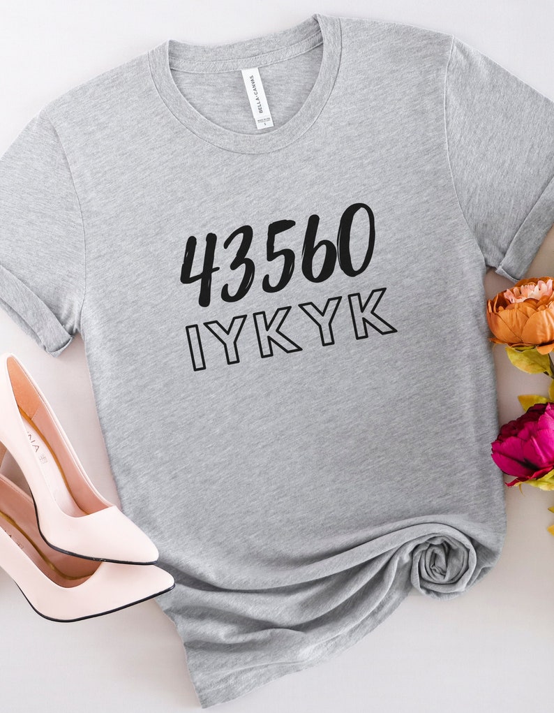 以下が含まれることがあります： 黒い文字で「43560 IYKYK」と書かれたグレーのTシャツ。