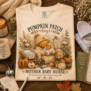 May include: A cream-coloured t-shirt featuring a graphic of a pumpkin-headed figure holding a swaddled baby in a chair, surrounded by pumpkins, a teddy bear, and foliage. The text reads PUMPKIN PATCH days, MOTHER BABY NURSE, and Nurturing New Beginnings.