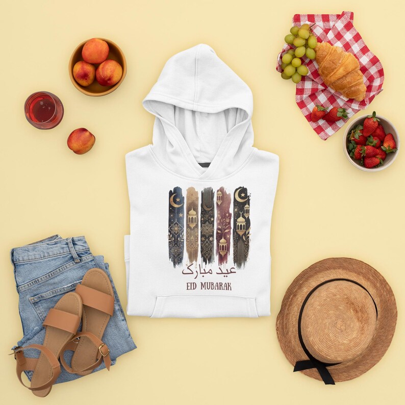 May include: White hooded sweatshirt with a colourful graphic design featuring Islamic lanterns, stars, and crescent moons. The text "Eid Mubarak" is written in Arabic and English.