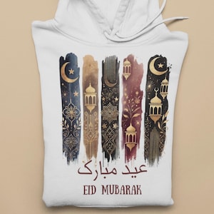 May include: White hoodie featuring a gold and black design of crescent moons, stars, and lanterns. The text "Eid Mubarak" is written in Arabic and English.