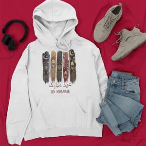 May include: White hooded sweatshirt featuring a graphic print of colourful Islamic art and the text "Eid Mubarak" in Arabic and English.