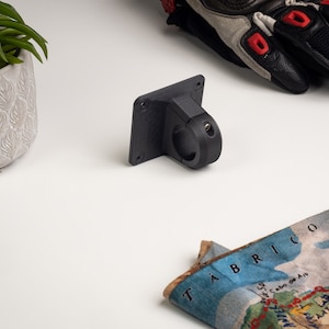 Könnte beinhalten: Ein schwarzer 3D-gedruckter Kamerahalter mit einer runden Klemme. Die Halterung ist an einer ebenen Fläche befestigt.