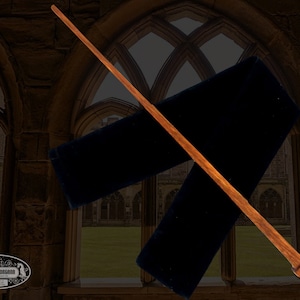 May include: A wooden wand with a brown finish and a carved handle. The wand is lying on a black velvet cloth. The background is a blurry image of a stone archway.