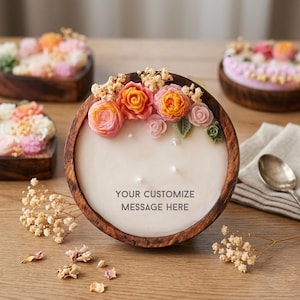 Peut inclure: Une bougie ronde dans un bol en bois, décorée d'accents floraux colorés. La bougie porte le texte "YOUR CUSTOMIZE MESSAGE HERE" et est entourée d'autres compositions florales.