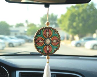 Può includere: Un ciondolo per auto rotondo e colorato con un design floreale. Il ciondolo è realizzato in legno e presenta un motivo dipinto nei toni del rosa, turchese e arancione. È appeso a una corda con una perla di legno e un nappa bianca.