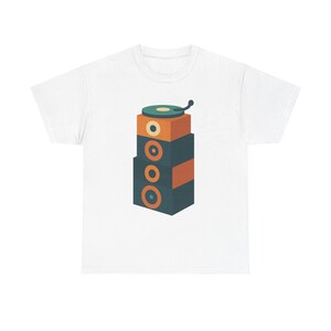 Puede incluir: Camiseta blanca con una ilustración apilada de un tocadiscos encima de unos altavoces. El diseño utiliza una paleta de colores retro de verde azulado, naranja y verde azulado oscuro. Los altavoces tienen agujeros circulares.