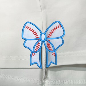 May include: A white fabric with a blue and red bow sewn on. The bow is shaped like a baseball with red stitching.