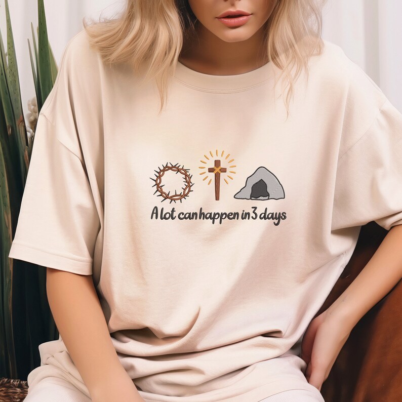 May include: A beige t-shirt with a graphic of a crown of thorns, a cross, and a tomb. The text "A lot can happen in 3 days" is printed below the graphic.