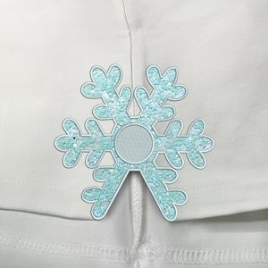 Puede incluir: Una camisa blanca con un adorno en forma de copo de nieve azul claro con detalles de purpurina.