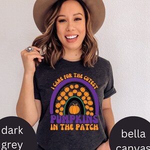 May include: Dark grey heather t-shirt with a colourful graphic. The design features a purple rainbow filled with orange pumpkins and the text "I care for the cutest pumpkins in the patch". The shirt is made of Bella Canvas material.