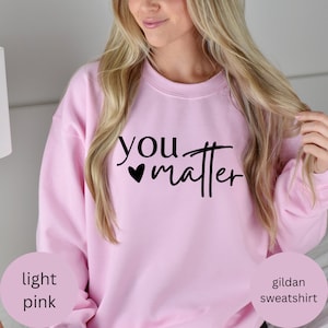 Op de afbeelding: Lichtroze Gildan sweatshirt met de tekst "you matter" in zwarte letters met een klein hartje voor het woord "matter".