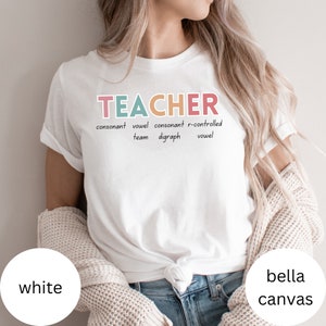 May include: White t-shirt with the word "TEACHER" in colorful letters and the definition of the word written below. The definition includes the words "consonant", "vowel", "digraph", and "r-controlled".