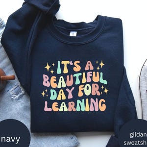 May include: Navy blue sweatshirt with the text "It's a beautiful day for learning" in colourful retro font.