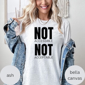 May include: A light gray long-sleeve shirt with the words "NOT ACCESSIBLE NOT ACCEPTABLE" in large black letters. The shirt is from Bella Canvas. The model is wearing a denim jacket.