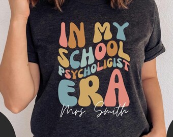 May include: A dark gray t-shirt with the text "In My School Psychologist Era" in colorful, retro-style lettering. The text "Mrs. Smith" is written in cursive below the main text.