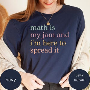 Op de afbeelding: Marineblauw t-shirt met de tekst "math is my jam and I'm here to spread it" in groen, roze en geel. Het shirt is gemaakt van Bella Canvas materiaal.