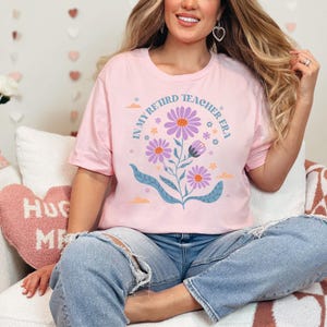 May include: A pink t-shirt with a floral design and the text "In My Retired Teacher Era".