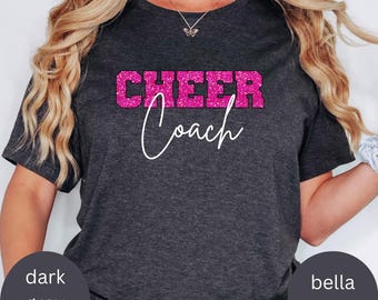 May include: A dark heather grey t-shirt with the text "CHEER COACH" in pink glitter lettering.