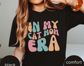 Könnte beinhalten: Schwarzes T-Shirt mit einem grafischen Design, das "In My Cat Mom Era" in bunten, Retro-Lettern zeigt. Eine kleine Katzenillustration ist im Design enthalten.