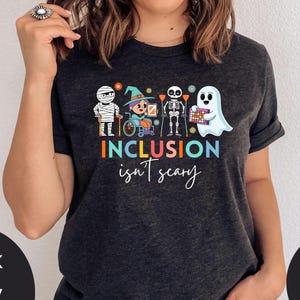 May include: A dark grey t-shirt featuring a graphic of a group of children dressed in Halloween costumes. The text "INCLUSION isn't scary" is printed below the graphic.