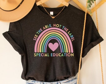 Może przedstawiać: Szary t-shirt z nadrukiem tęczy i serca. Tekst na koszulce brzmi "See the able, not the label, Special Education".