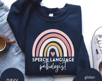May include: Navy blue Gildan sweatshirt with a rainbow design and the text "Speech Language Pathologist" in white. A small heart is in the center of the rainbow.