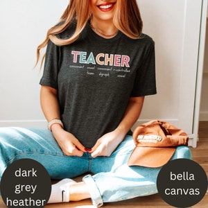 May include: A dark heather grey t-shirt with the word "TEACHER" written in colorful letters. The word is defined with the words "consonant", "vowel", "consonant", "r-controlled", "team", "digraph", and "vowel".
