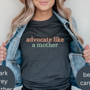 Könnte beinhalten: Ein dunkel-melierter grauer T-Shirt mit dem Text "advocate like a mother" in rosa, grün und orangefarbener Schrift.