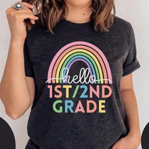May include: A dark grey t-shirt with a rainbow graphic and the text "hello 1st/2nd grade".