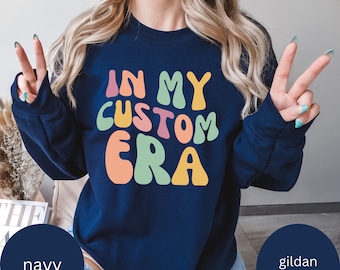 Può includere: Felpa blu navy con il testo "In My Custom Era" in lettere colorate in stile retrò.