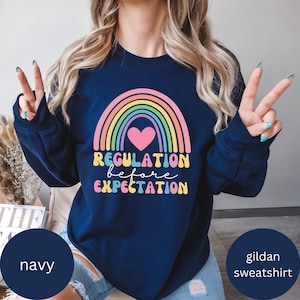 May include: Navy blue Gildan sweatshirt featuring a rainbow and heart graphic. The text "Regulation before Expectation" is printed in a retro font.