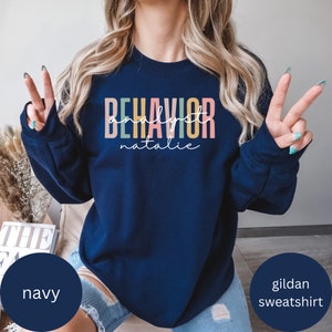 Puede incluir: Sudadera azul marino Gildan con el texto "BEHAVIOR analyst natalie" en colores arcoíris.