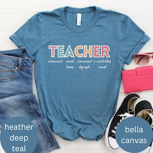 May include: A teal blue t-shirt with the word "TEACHER" in colorful letters. The word is broken down into its parts of speech, with the text "consonant vowel consonant r-controlled team digraph vowel" underneath.