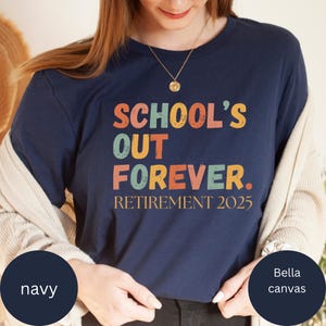 May include: Navy blue t-shirt with the text "SCHOOL'S OUT FOREVER. RETIREMENT 2025" in orange, yellow, and teal lettering. The shirt is made of Bella Canvas material.